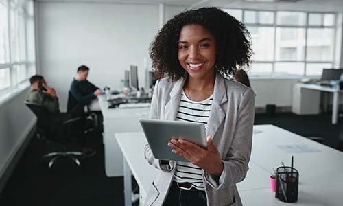 Woman in a blazer and striped shirt smiles in a professional workplace as she streamlines product management.