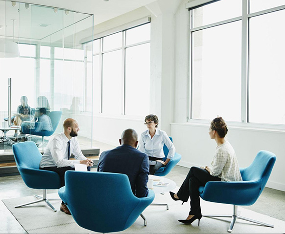 Four coworkers sit in blue, round chairs to discuss a project related to their critical industry experience with major media companies.